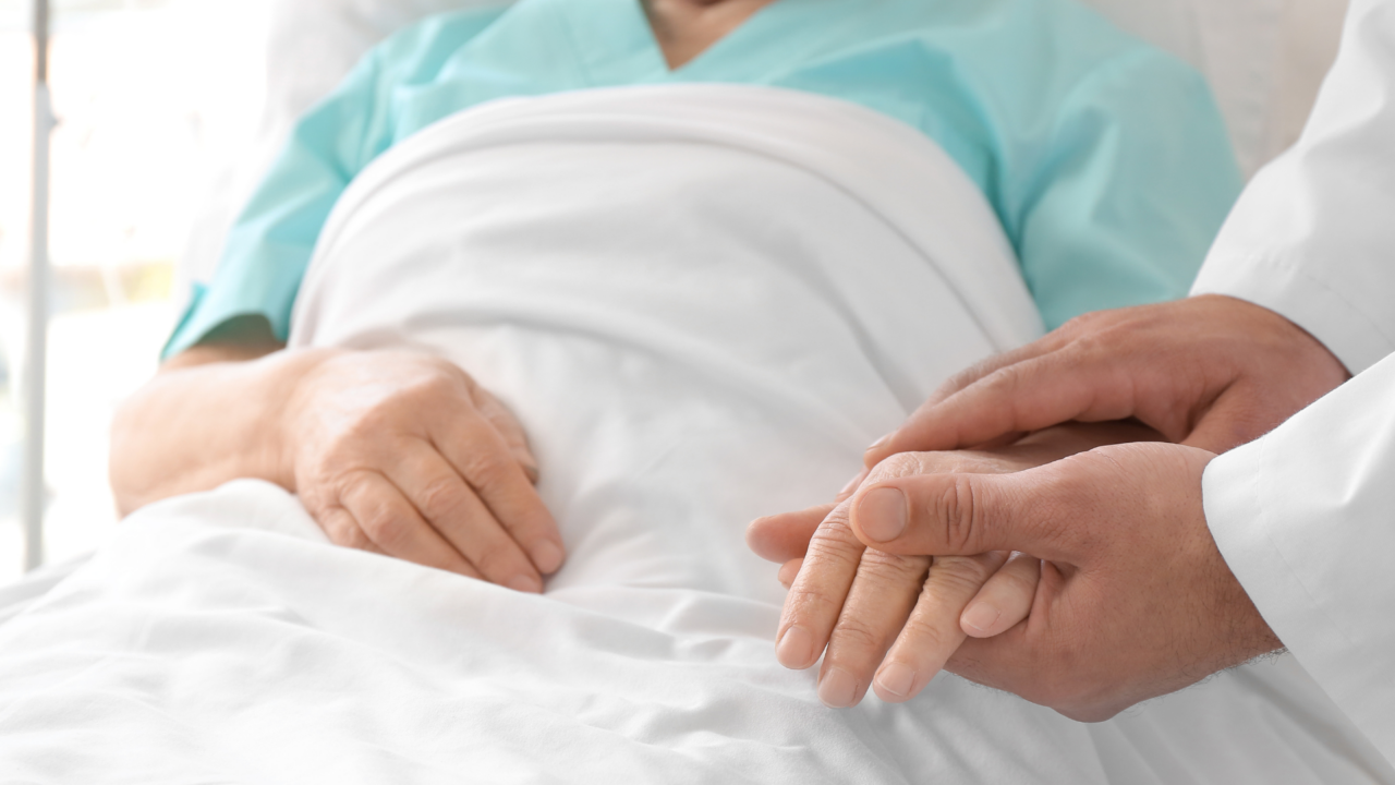 The image shows a close-up of a healthcare scene where a patient, lying in bed, is being comforted by a medical professional.