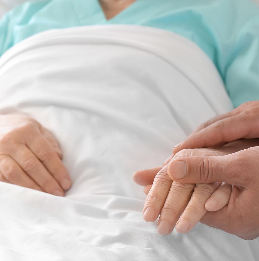 The image shows a close-up of a healthcare scene where a patient, lying in bed, is being comforted by a medical professional.