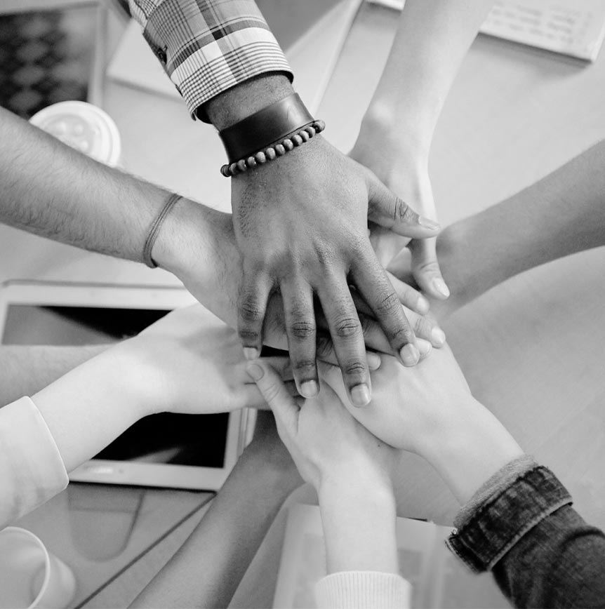 Black and white image of multiple hands from different individuals coming together in a pile, symbolizing teamwork and unity.