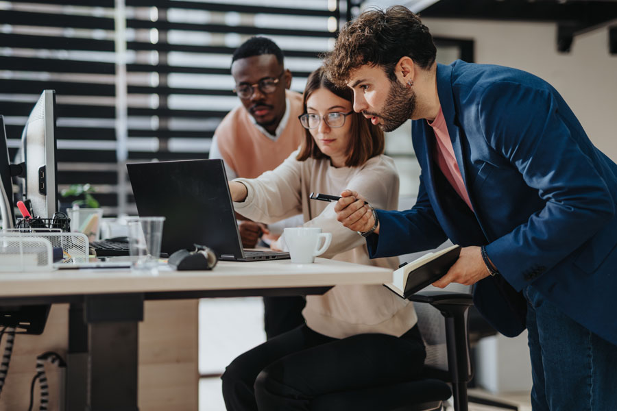 Three IT professionals collaborating in a modern office, reviewing a cloud project on a laptop.