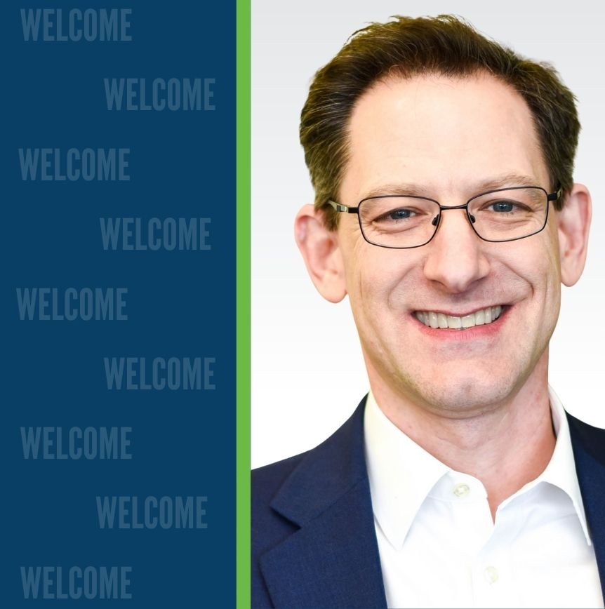 Jason Balser, Senior Director of AI & Data Strategy at RELI Group, in front of a welcome banner.