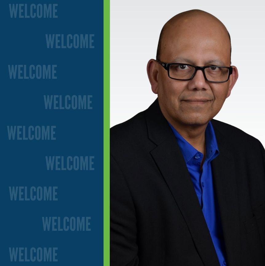 Professional headshot of Sarjoo Shah in a black blazer and blue shirt, set against a blue background with vertically repeated 'WELCOME' text and a green divider.