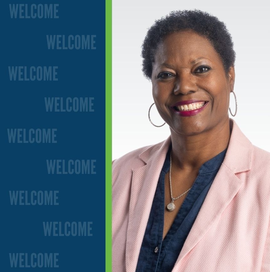 Rhonda White, smiling in a pink blazer, stands beside a blue background with repeated “WELCOME” text.