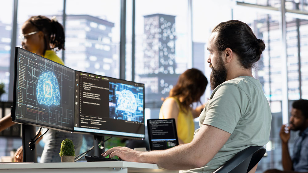 AI engineer working at a desk with dual monitors displaying AI brain graphics and code in a modern office setting.