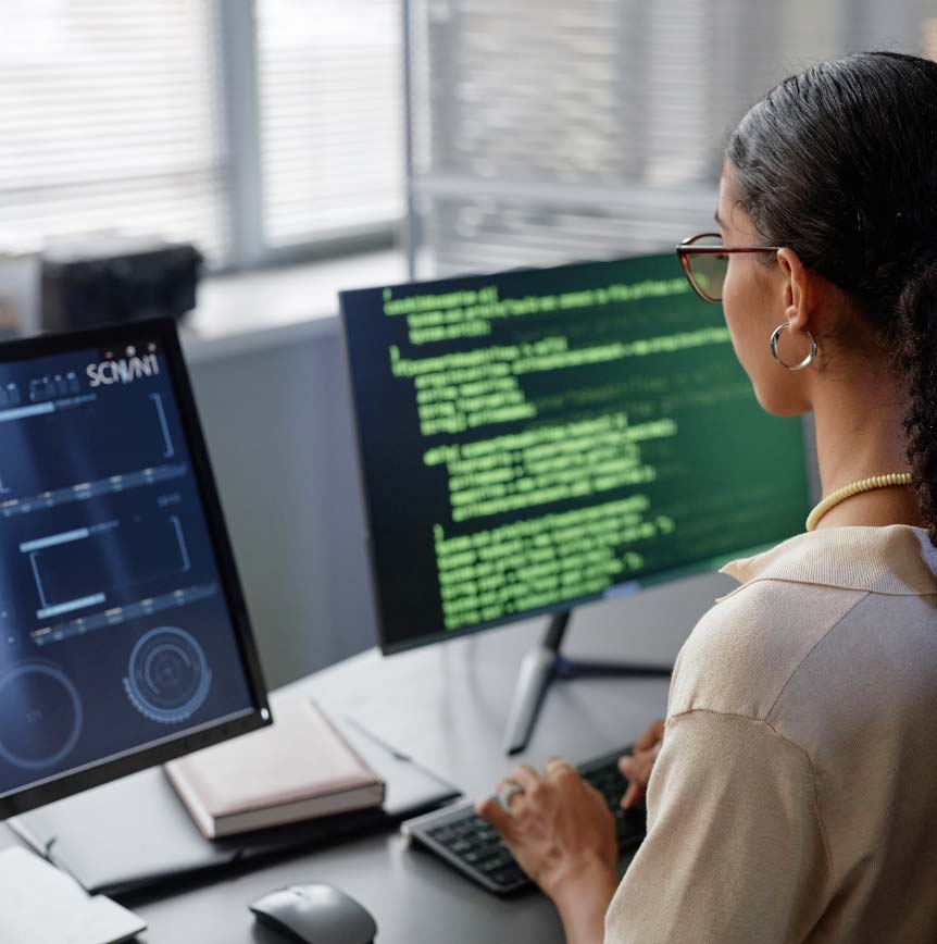 Person sitting at desk with dual monitors writing code.