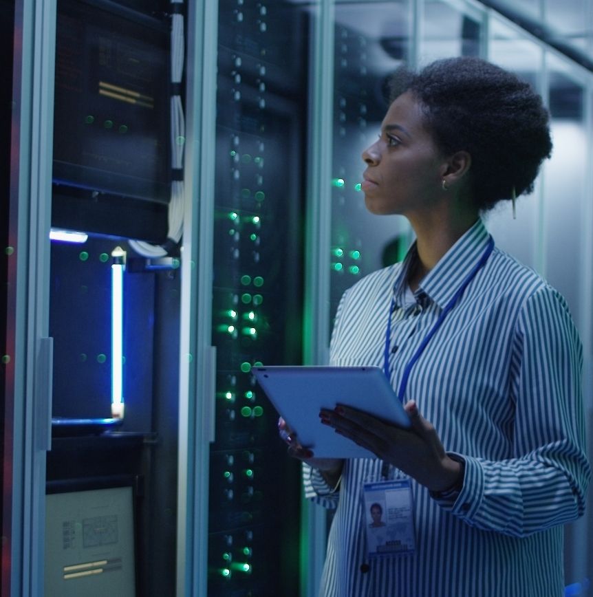 A technician holding a tablet inspects illuminated server racks in a data center.