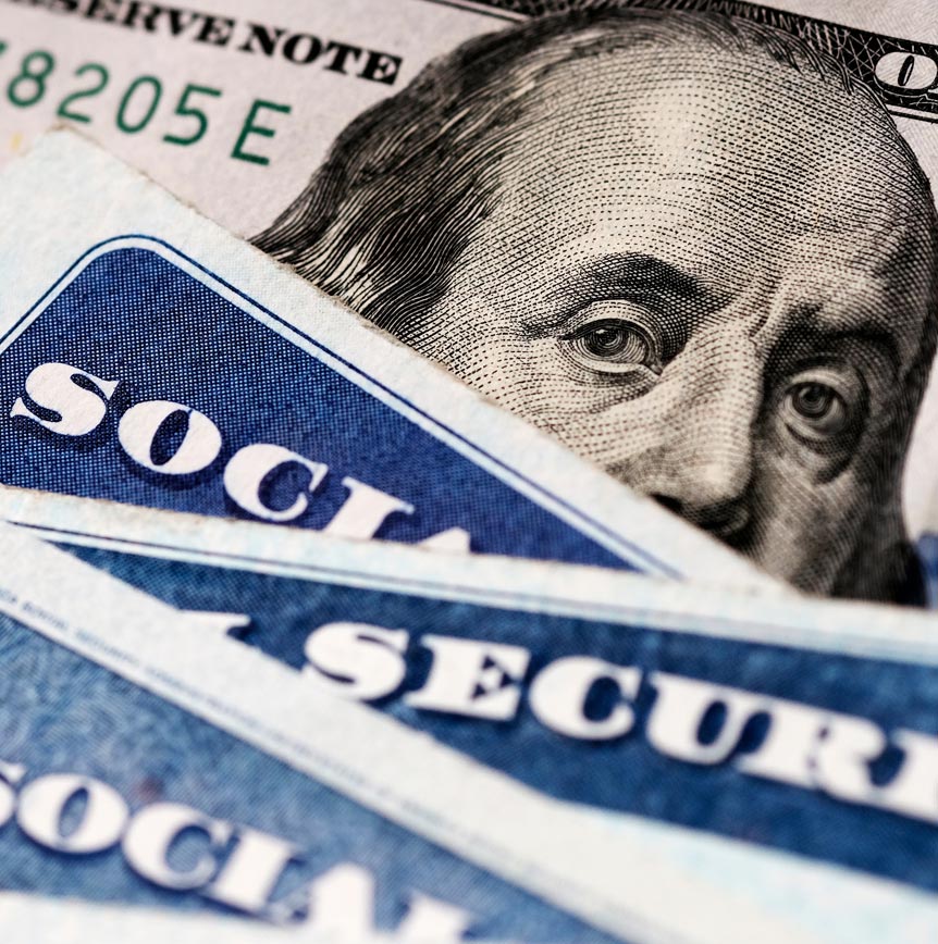 Several Social Security cards laid over a U.S. hundred‑dollar bill representing entitlement programs