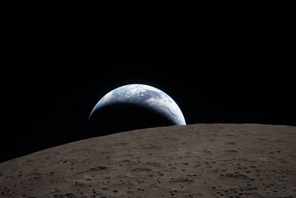 View from the Moon’s surface with Earth rising over the horizon with space in the background.