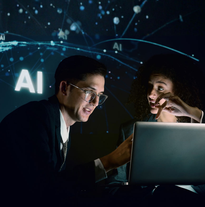Two employees collaborating over a laptop in a dark room with AI network graphics projected in the background
