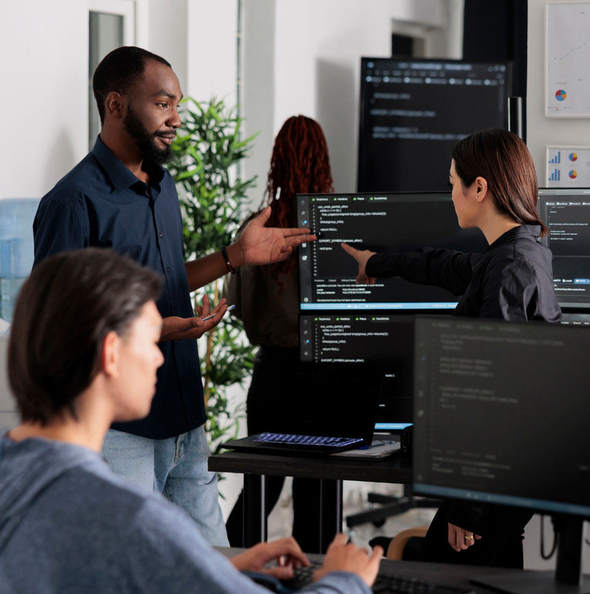 Software engineering team collaborating in office, reviewing code across multiple monitors and discussing implementation details