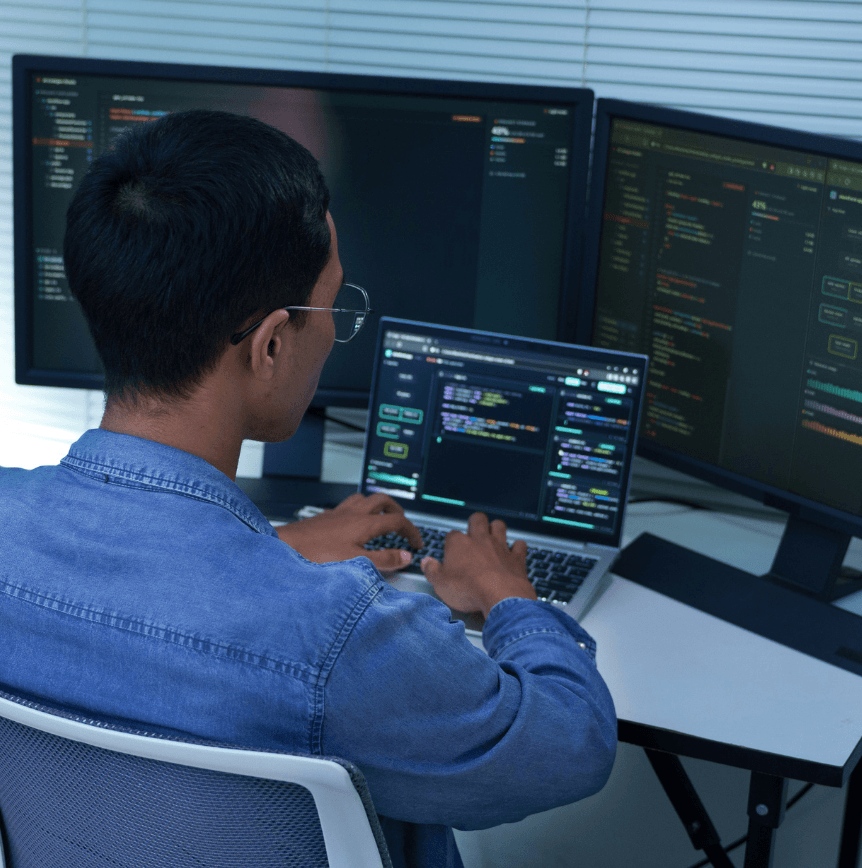 Developer working at a laptop surrounded by code-filled monitors representing AI model development and analysis.