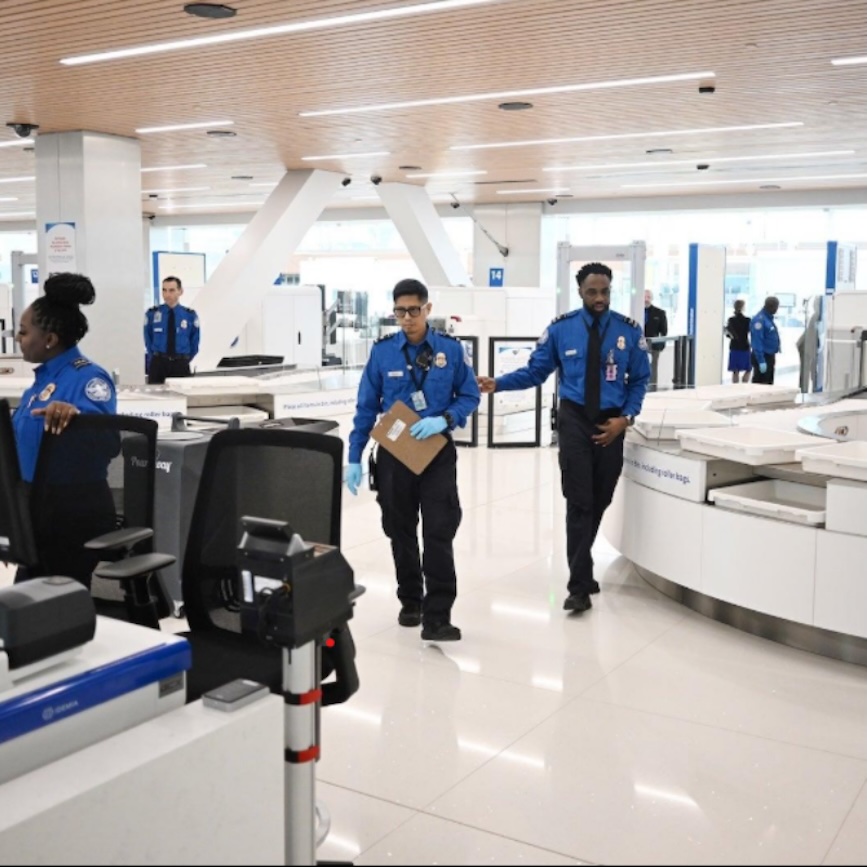 TSA officers work among screening stations and security equipment at a modern airport checkpoint.