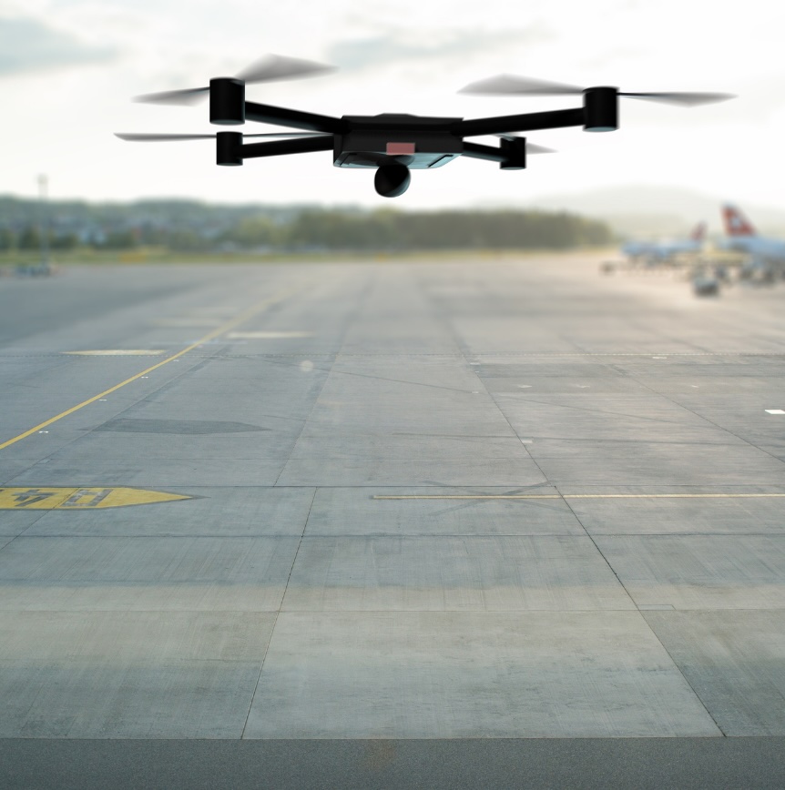 Drone flying above an airport runway with aircraft visible in the background.